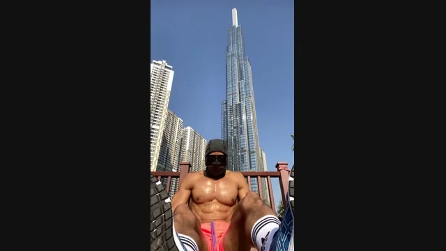 Low-angle daylight photograph of a masked athlete seated outdoors, with high-rise buildings behind him.