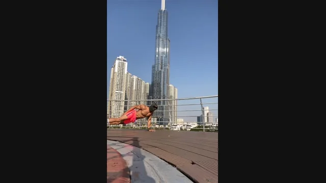 Masked athlete holding a side-plank position on an outdoor deck, with high-rise buildings in the background.