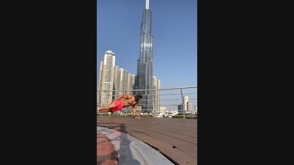 Masked athlete holding a side-plank position on an outdoor deck, with high-rise buildings in the background.